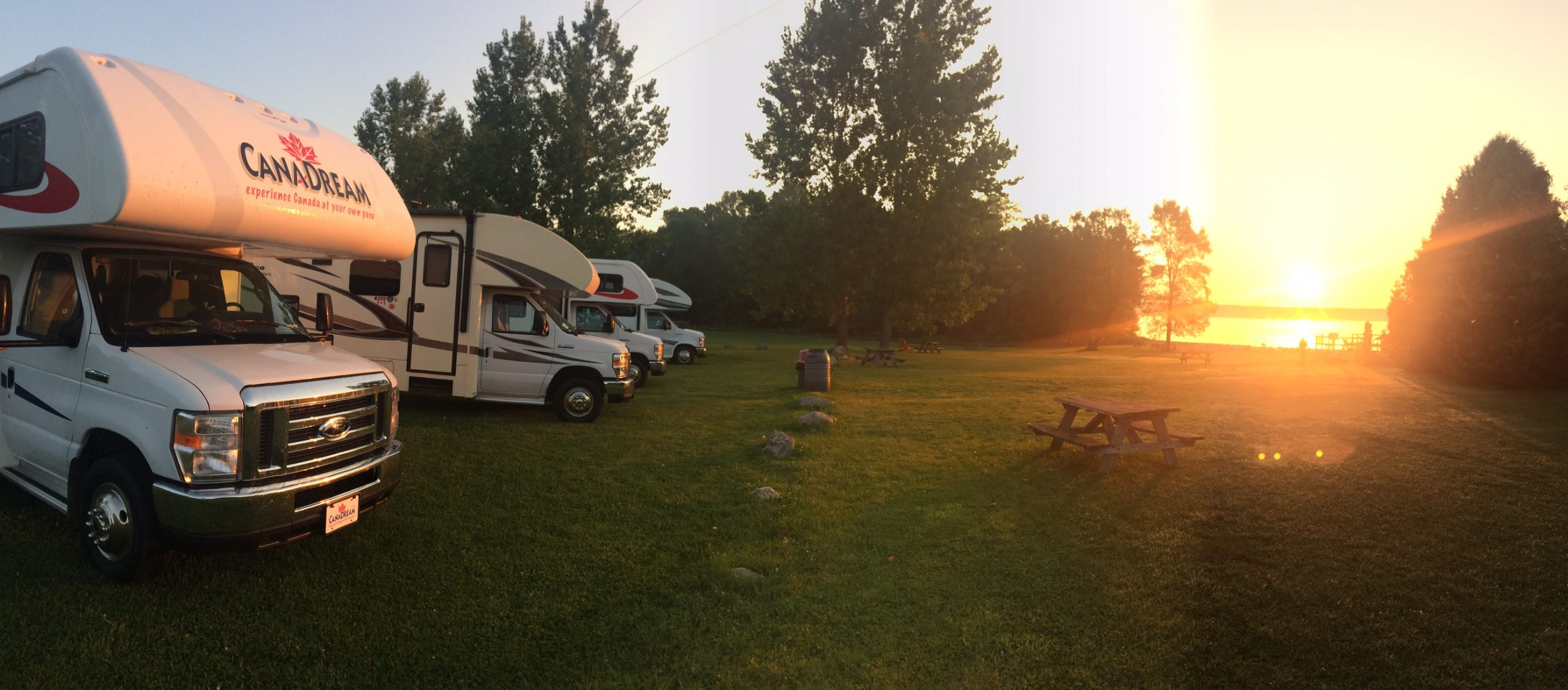 A line of RVs parked at a campsite, at sunset