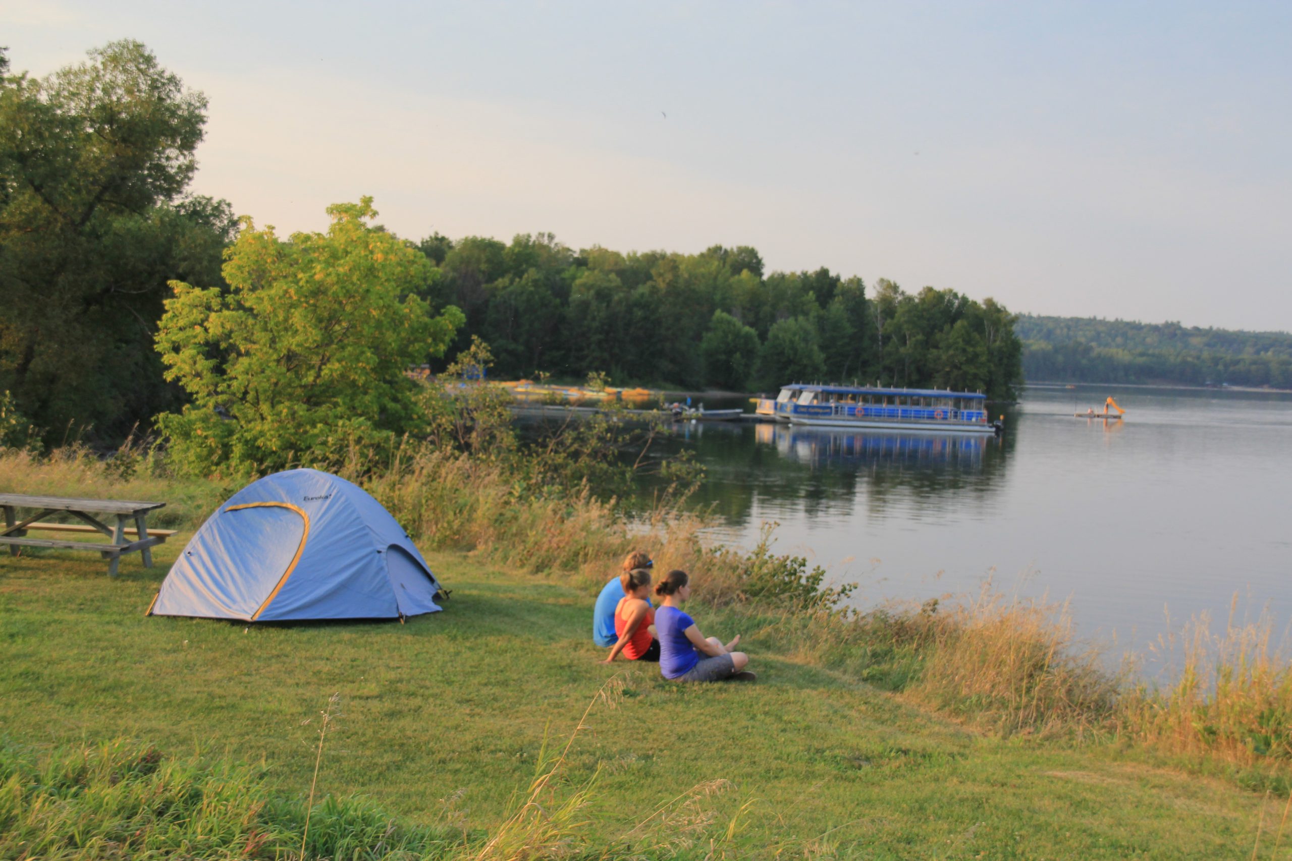 Three people sitting next to a tent by a lake