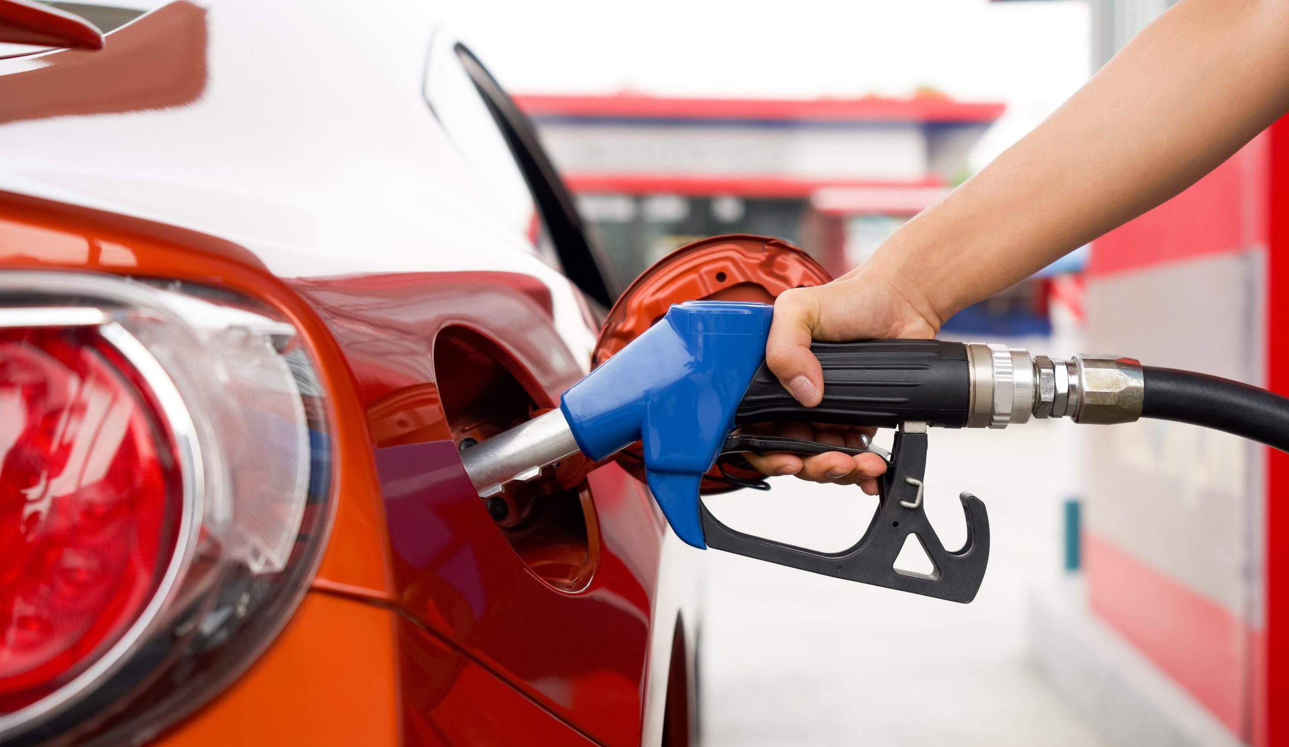 Gas station worker's hand holding gas pump, filling up red car tank