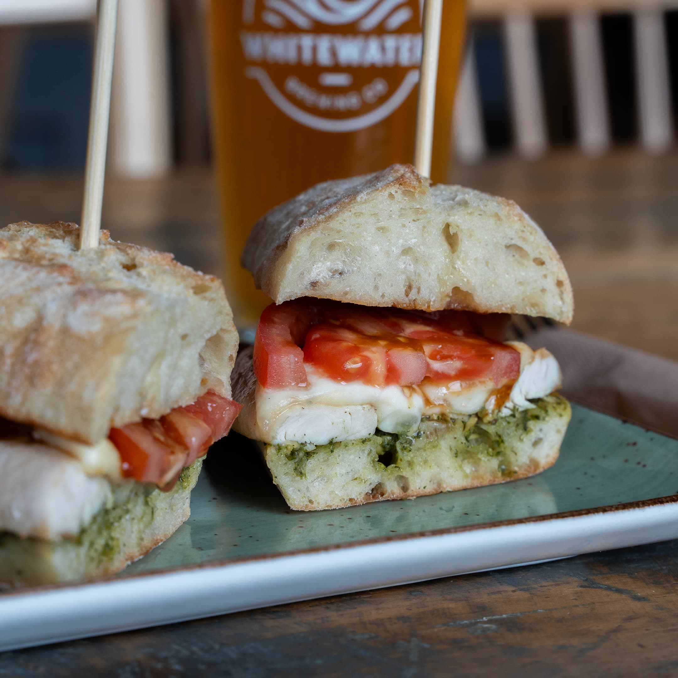 Two halves of a chicken caprese sandwich and a Whitewater beer