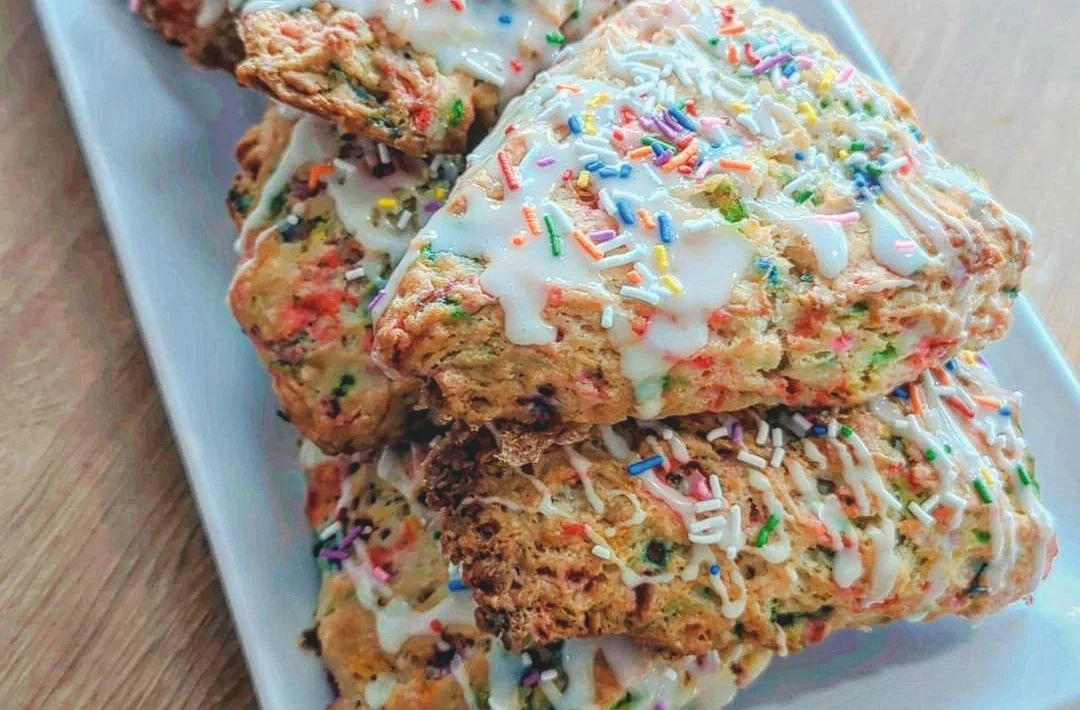 A plate of scones with icing and rainbow sprinkles