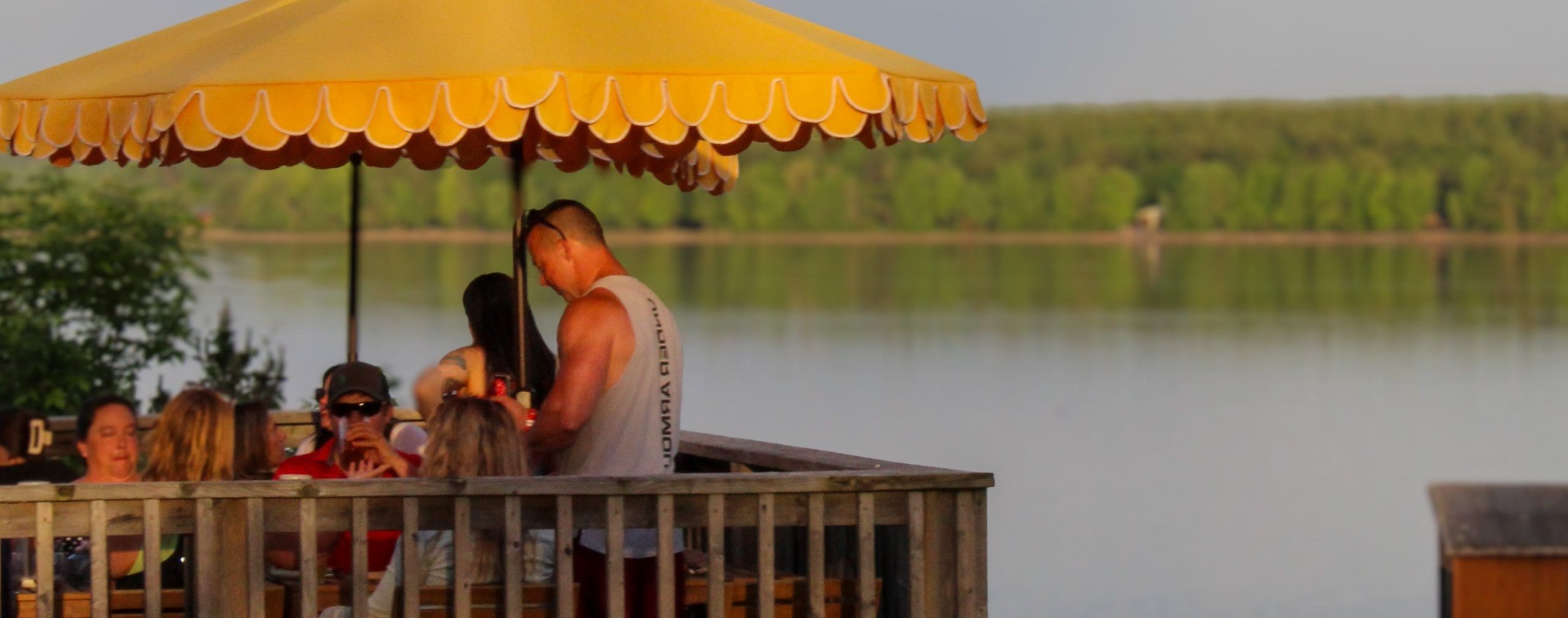 A patio by the water, with several people under a yellow shade